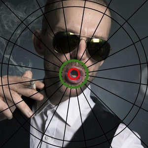 May include: A man wearing sunglasses and a white shirt with a black vest is shown in front of a dartboard. The bullseye of the dartboard is centered on his mouth.