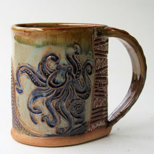 May include: A ceramic mug with a brown, green, and blue glaze. The mug features a detailed design of an octopus with tentacles.