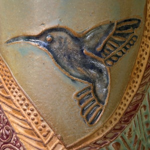May include: A ceramic vase with a blue and brown hummingbird design. The vase has a textured surface with a brown and gold pattern.