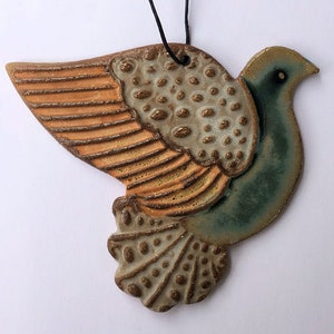 May include: A ceramic dove ornament with a teal blue body, orange and brown wings, and a textured surface. The dove is hanging from a black string.