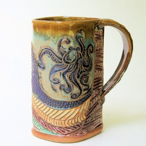 May include: A ceramic mug with a brown, blue, and green glaze. The mug features a raised design of an octopus with tentacles. The mug has a handle and is perfect for holding a hot beverage.