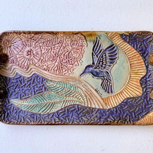 May include: A ceramic serving tray with a blue bird design. The tray has a textured surface with floral and leaf patterns in shades of brown, pink, green, and purple.