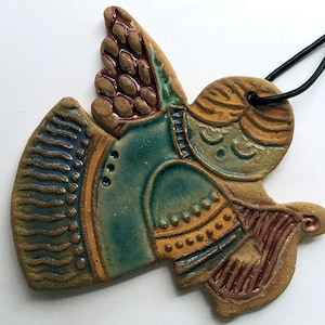 May include: A ceramic angel ornament with a blue, yellow, and brown glaze. The angel has wings, a halo, and a trumpet. The ornament is attached to a black cord.