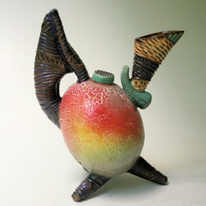 May include: A quirky ceramic teapot with a textured, brown handle and a colourful, speckled body. The teapot has a unique spout and a green, textured lid.