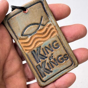 May include: A ceramic tile with a blue and brown glaze. The tile has a fish symbol and the words "KING of KINGS" in black lettering.