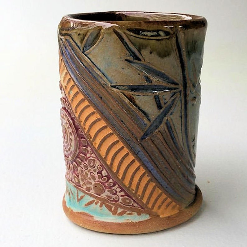 May include: A ceramic mug with a colorful, geometric design. The mug is decorated with brown, orange, blue, and pink patterns.