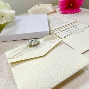 Magnifique échantillon de faire-part de mariage. Avec de la dentelle de style vintage, un ruban plissé et une décoration de perles. Comprend une carte RSVP, des informations sur les clients et un menu.