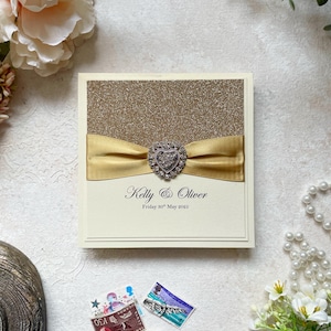 Glitzer-Hochzeitseinladungs-Muster. Mit goldenem Satinband & Herzverzierung. Inklusive Antwortkarte, Gästeinfo und Menü.