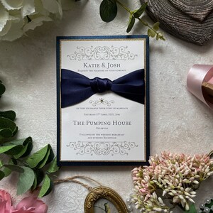 Échantillon d’invitation de mariage fait à la main. Invitation plate avec ruban et enveloppe. Marine et or 5x7 pouces. Carte pailletée et ruban de satin. Comprend RSVP