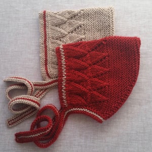 May include: Two knitted baby bonnets, one red and one beige, with matching ties. The bonnets have a cable knit pattern and are trimmed with a contrasting color.