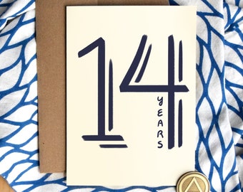 May include: A white card with the number 14 in large, dark blue font. The word "years" is written vertically in smaller dark blue font next to the number. The card is on a blue and white patterned fabric.