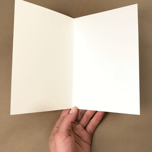 May include: A blank white card folded in half. The card is held in a hand.