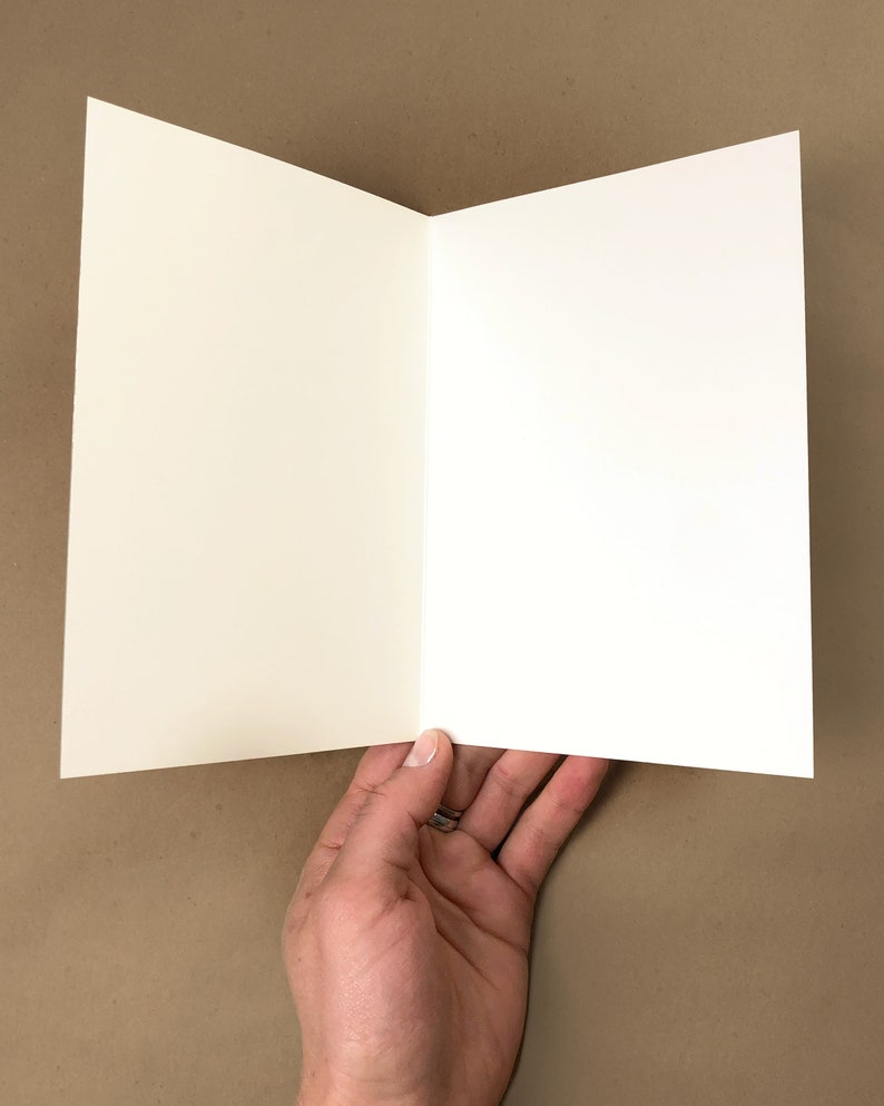 May include: A blank white card folded in half. The card is held in a hand.
