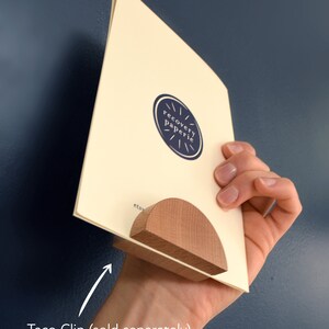 May include: A wooden taco clip with magnets embedded in the wood to hold the pieces together. The clip is holding a card with the text "recovery paperie" on it.