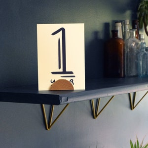 May include: A black shelf with gold metal brackets, a wooden number holder with the number "1" written on a yellow card, and a few glass bottles on the shelf.