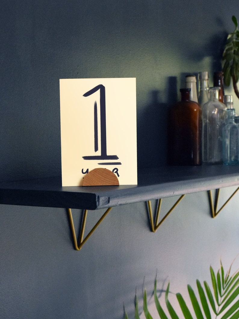 May include: A black shelf with gold metal brackets, a wooden number holder with the number "1" written on a yellow card, and a few glass bottles on the shelf.