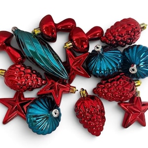 May include: A collection of shiny Christmas ornaments in red and teal. The set includes red mushroom-shaped pieces, red stars, red pinecone-textured baubles, a long teal finial, and round, ribbed teal ornaments with gold-tone metal caps.
