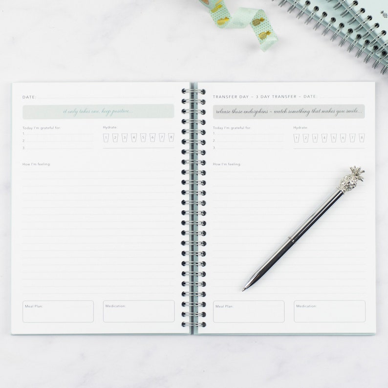 The ivf journey planner open on a table showing a double page spread of the daily pages. A pineapple shaped biro lays on top of one of the pages.