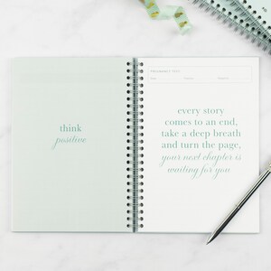 ivf journey planner laying on a table open at the test day page, the quotes read 'think positive' and 'every story comes to an end, take a deep breath and turn the page, your next chapter is waiting for you.