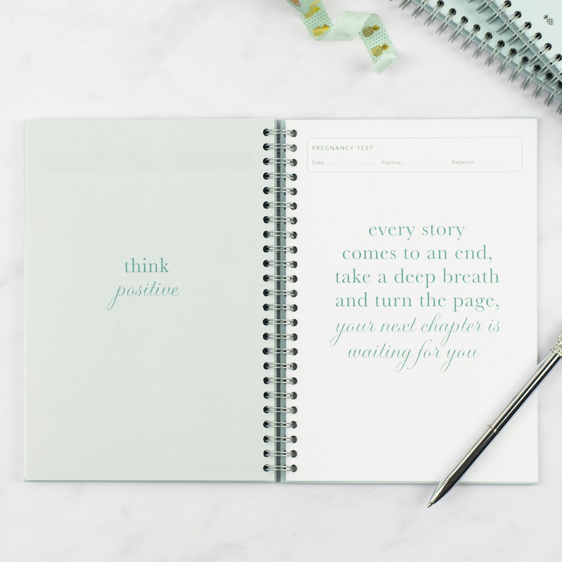 ivf journey planner laying on a table open at the test day page, the quotes read 'think positive' and 'every story comes to an end, take a deep breath and turn the page, your next chapter is waiting for you.