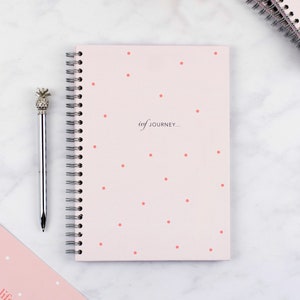 Flat lay image of the cover of the pink spot ivf planner, it details the wiro binding and the text on the cover which says ivf journey.