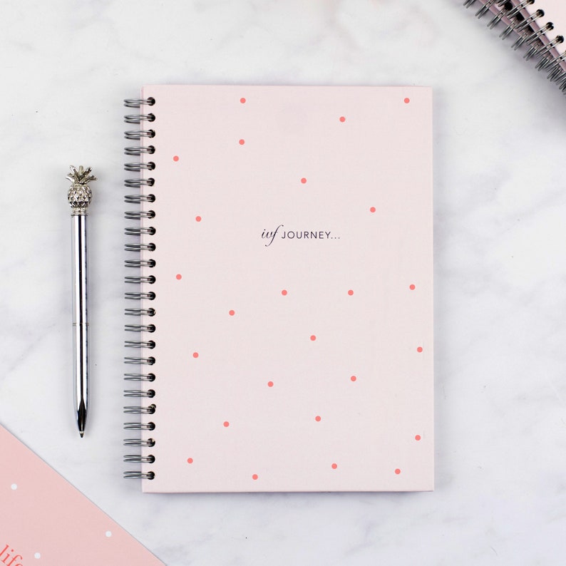 Flat lay image of the cover of the pink spot ivf planner, it details the wiro binding and the text on the cover which says ivf journey.