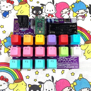 May include: A purple MIDI controller circuit board featuring a green microcontroller, a black battery holder, and eighteen colourful square keycaps labelled with symbols and function keys. The board includes printed text such as MIDI.OUT, TAMAGOTCHI, and PARADISE 64.