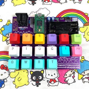 Può includere: Una scheda a circuito stampato per controller MIDI viola con una griglia di tasti colorati etichettati con lettere e numeri. La scheda include un microcontrollore, un vano batteria e testo stampato tra cui "TAMAGOTCHI PARADISE 64" e "ULTRA HEADY VIBES".