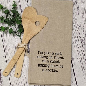 May include: A beige kitchen towel with the text "I'm just a girl, sitting in front of a salad, asking it to be a cookie." printed in black.