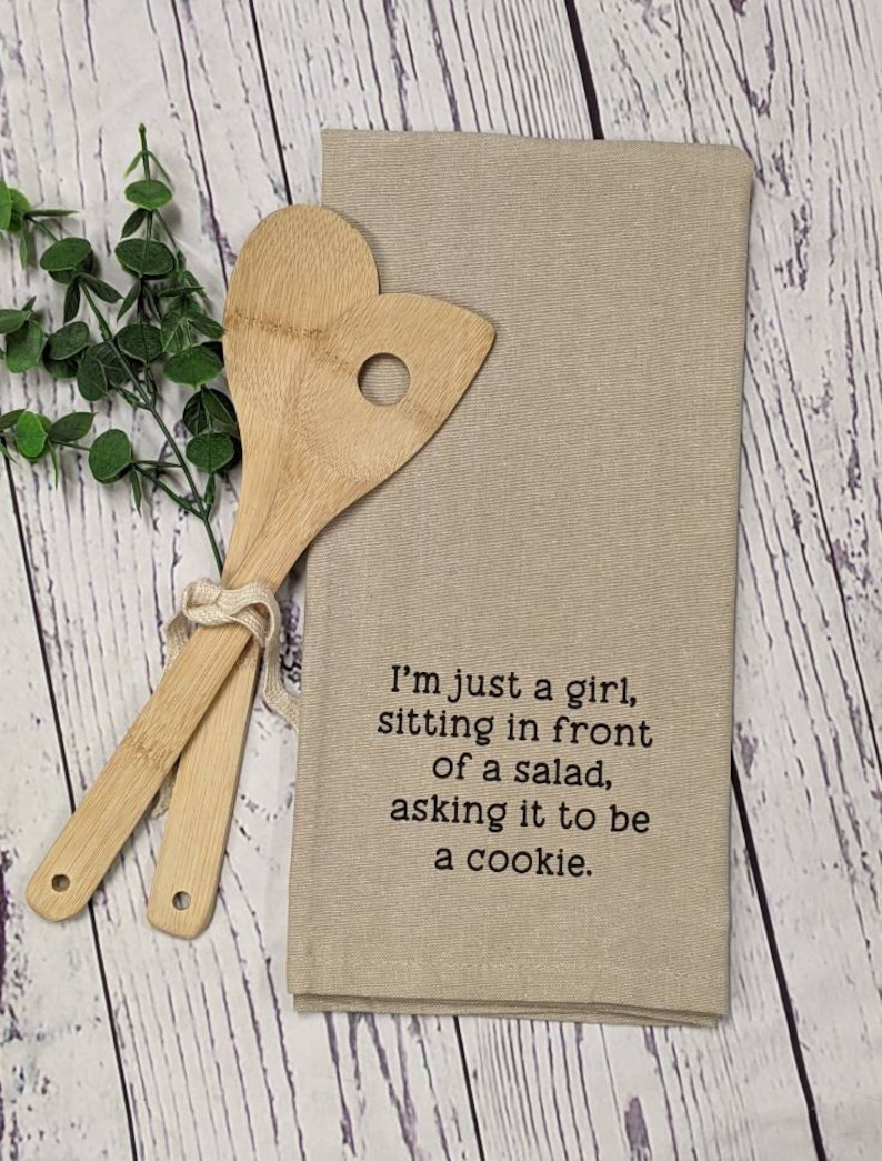 May include: A beige kitchen towel with the text "I'm just a girl, sitting in front of a salad, asking it to be a cookie." printed in black.