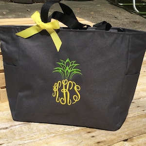 May include: A gray canvas tote bag with a yellow ribbon, a green pineapple design, and the monogram "KKS" in yellow.
