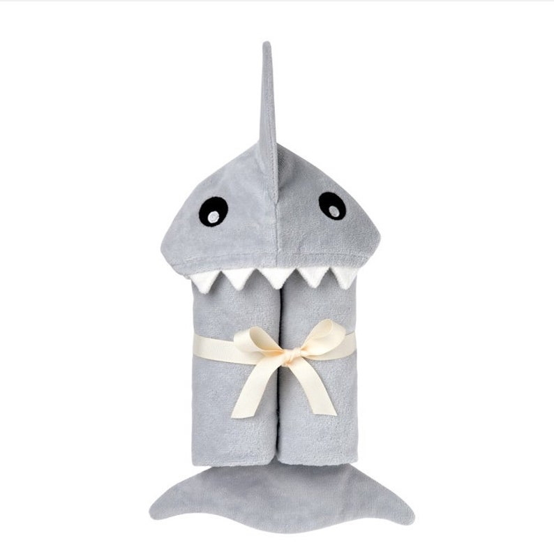 May include: A gray hooded towel shaped like a shark with a white mouth and black eyes. The towel is tied with a cream-colored ribbon.