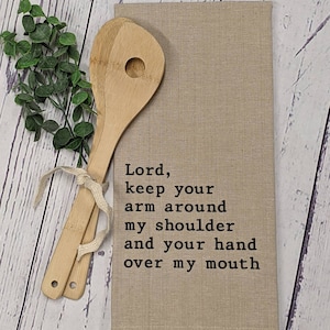 May include: A beige kitchen towel with the text "Lord, keep your arm around my shoulder and your hand over my mouth" printed in black.