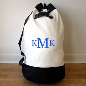 May include: White canvas laundry bag with black trim and blue monogram "KMK".
