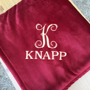 May include: A red velvet throw blanket with a gold embroidered monogram "K" and the name "KNAPP".