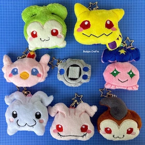 May include: A collection of ten plush toys, each with a different design. The toys are all in various colors, including green, yellow, blue, pink, and gray. The toys are all about 4 inches tall and have a variety of features, such as eyes, mouths, and ears. The toys are all attached to keychains, making them perfect for carrying around or hanging on a bag.