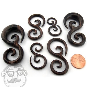 May include: Set of six brown wood spiral ear gauges. The gauges are in various sizes and are made of a dark wood with a natural grain pattern.