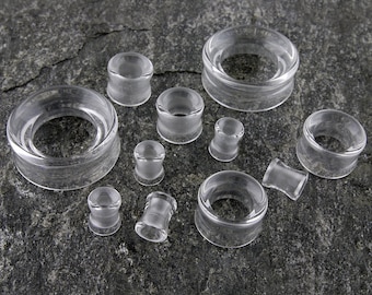 May include: A set of clear glass ear gauges of various sizes. The gauges are round and have a smooth, polished finish.