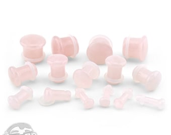 May include: A set of pink stone ear gauges in various sizes. The gauges are made of a smooth, polished stone and have a slightly translucent appearance.