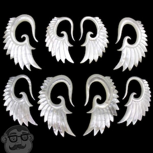 May include: Set of six white mother of pearl ear gauges with a wing design. Each gauge features a curved, spiral shape with a wing design on either side.