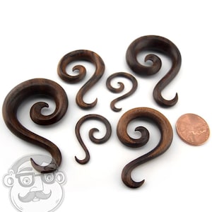 Könnte beinhalten: Ein Satz von sechs Holz-Ohrenstreckern mit einem Spiraldesign. Die Strecker sind aus dunkelbraunem Holz gefertigt und haben eine natürliche Oberfläche.