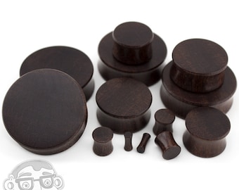 May include: A set of brown wooden ear gauges in various sizes. The gauges are made of a dark wood with a smooth finish.