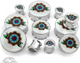 May include: A collection of silver-colored ear gauges with a white face featuring a red, yellow, and blue floral design. The gauges vary in size and are arranged on a white background. The floral design is surrounded by green leaves.
