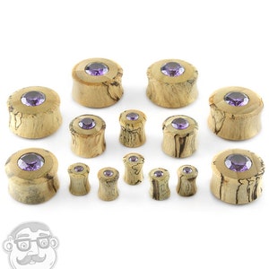 May include: A set of wooden ear gauges with purple gemstone accents. The gauges are available in a variety of sizes.