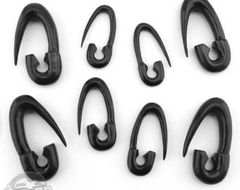 May include: Eight black safety pin style ear gauges. The gauges are made of a smooth, shiny material and have a curved shape.