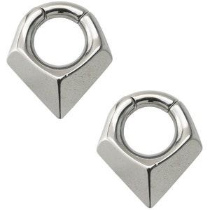 May include: Two silver-colored, geometric body jewelry pieces. Each piece features a rounded ring connected to a diamond-shaped base. The metal has a polished, reflective surface. The design is modern and minimalist.