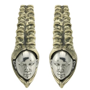 May include: A pair of silver and gold-toned earrings. Each earring features a stylized face with a smooth silver finish, framed by a gold-toned, textured design. The earrings have a long, vertical shape.