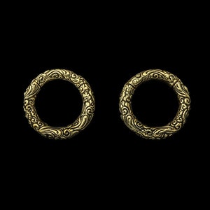 May include: Two gold-coloured metal rings with intricate, swirling designs. The rings are smooth and shiny, and the designs are raised and detailed.