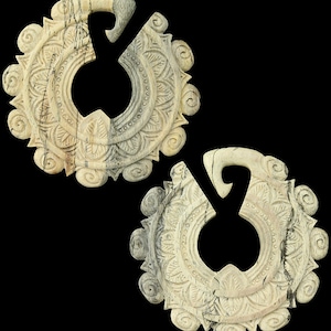 May include: Two cream-colored, carved earrings with intricate floral and swirl designs. Each earring has a circular shape with a large opening and a curved hook. The earrings are set against a black background.