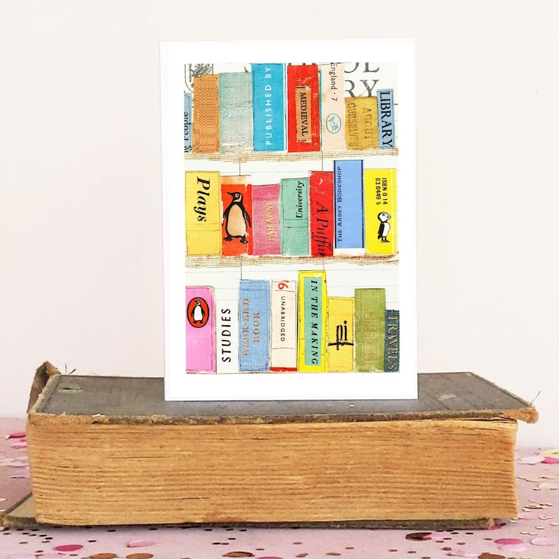 May include: A greeting card featuring a collage of colorful book spines arranged on shelves. The card includes titles like "Plays," "Studies," and "Medieval." A vintage book serves as a base for the card, with a pink and white background.